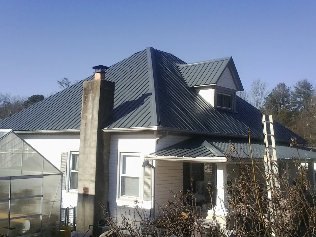 Dark blue standing seam metal roof on a white farmhouse with dormer — Slate & Tile Roof Repair by Roofing Brothers in Home