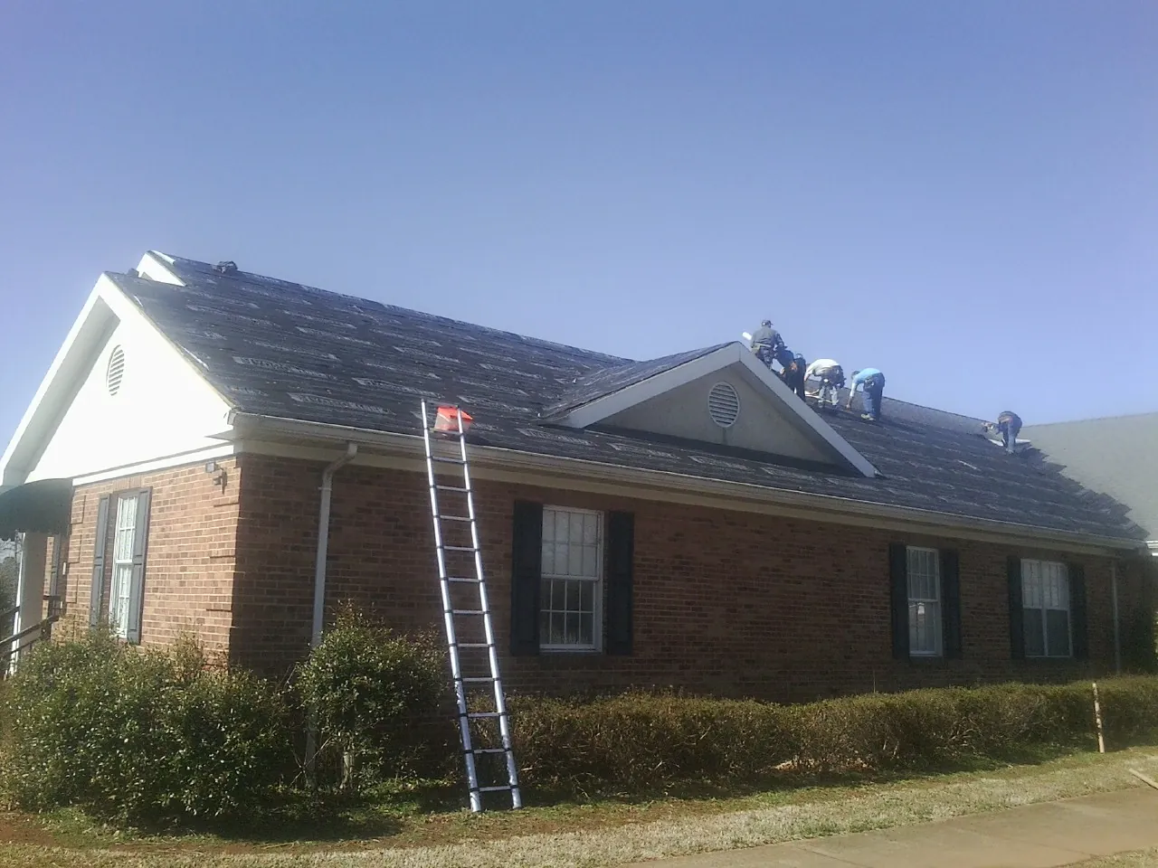 Crew tearing shingles off a brick ranch roof with a ladder set — Emergency Roof Repair work by our crew in Home