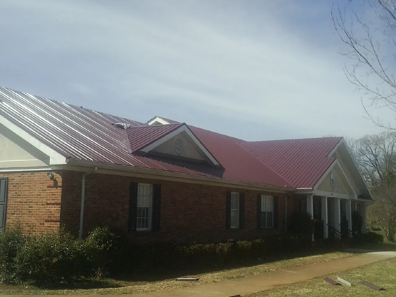 Red metal roof with gabled entries on a long brick building, from a Hail Damage Roof Repair job in Home