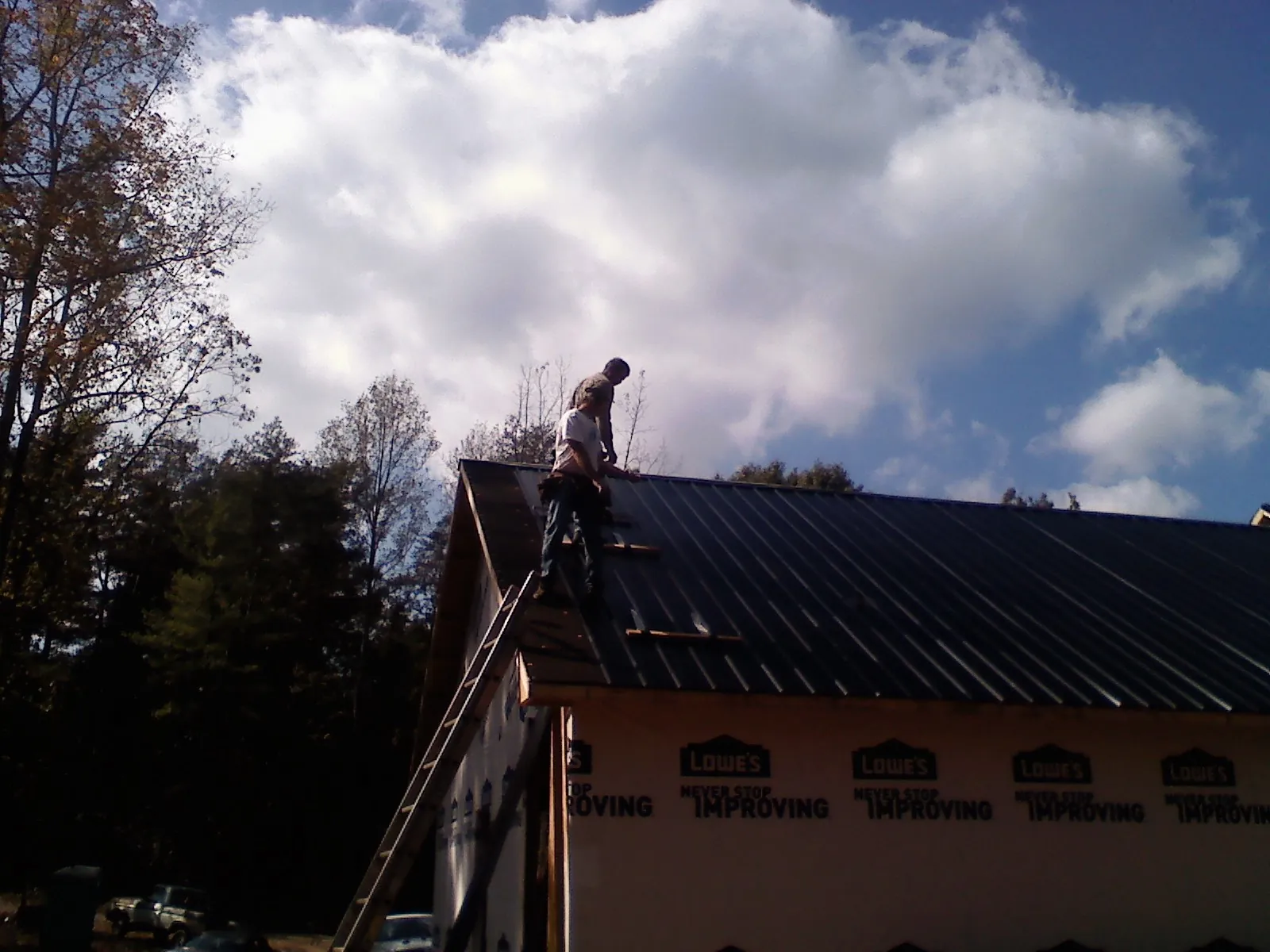 Roofer fastening dark metal panels high against a cloudy sky, from a Roof Inspection job in Home