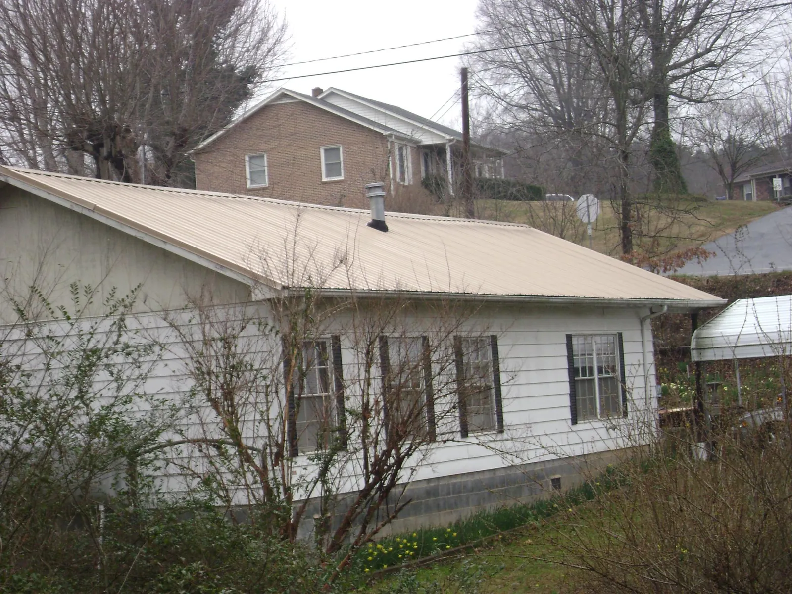 Tan metal roof on a white sided house set into a hillside — Commercial Roofing by Roofing Brothers in Home