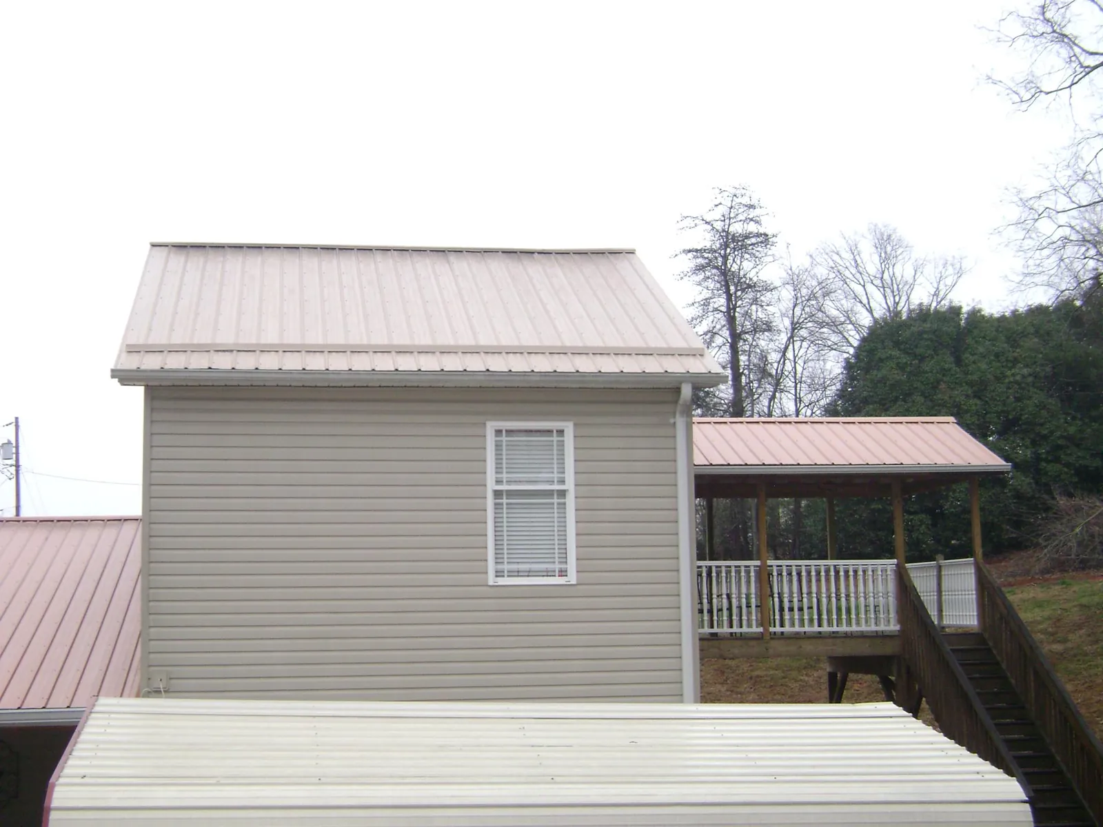 Tan metal roofs on a two story addition and attached porch, from a Roof Replacement job in Home