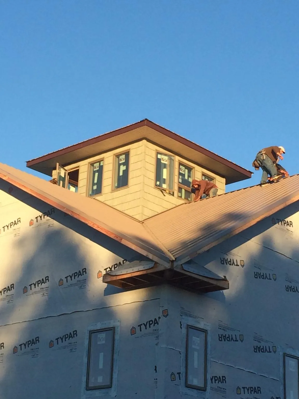 Roofers working around a rooftop cupola on a new metal roof at sunset — Roof Waterproofing in Home by Roofing Brothers